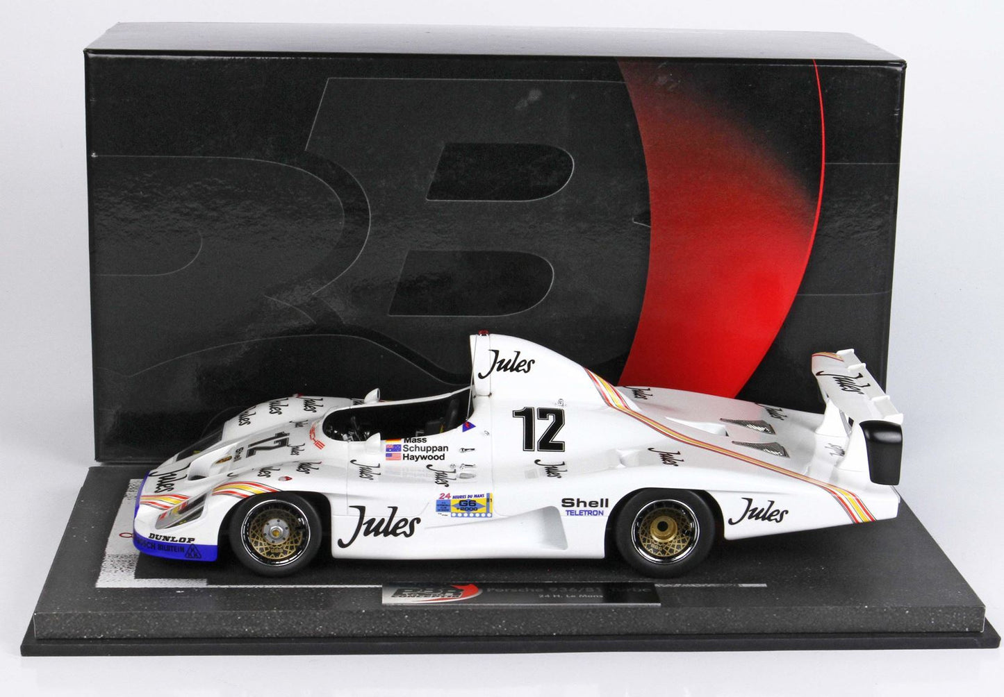 Modellino di auto da corsa Porsche 962 bianca con marchio Jules e numero 12, in una scatola nera e rossa, disponibile su Vroomi.