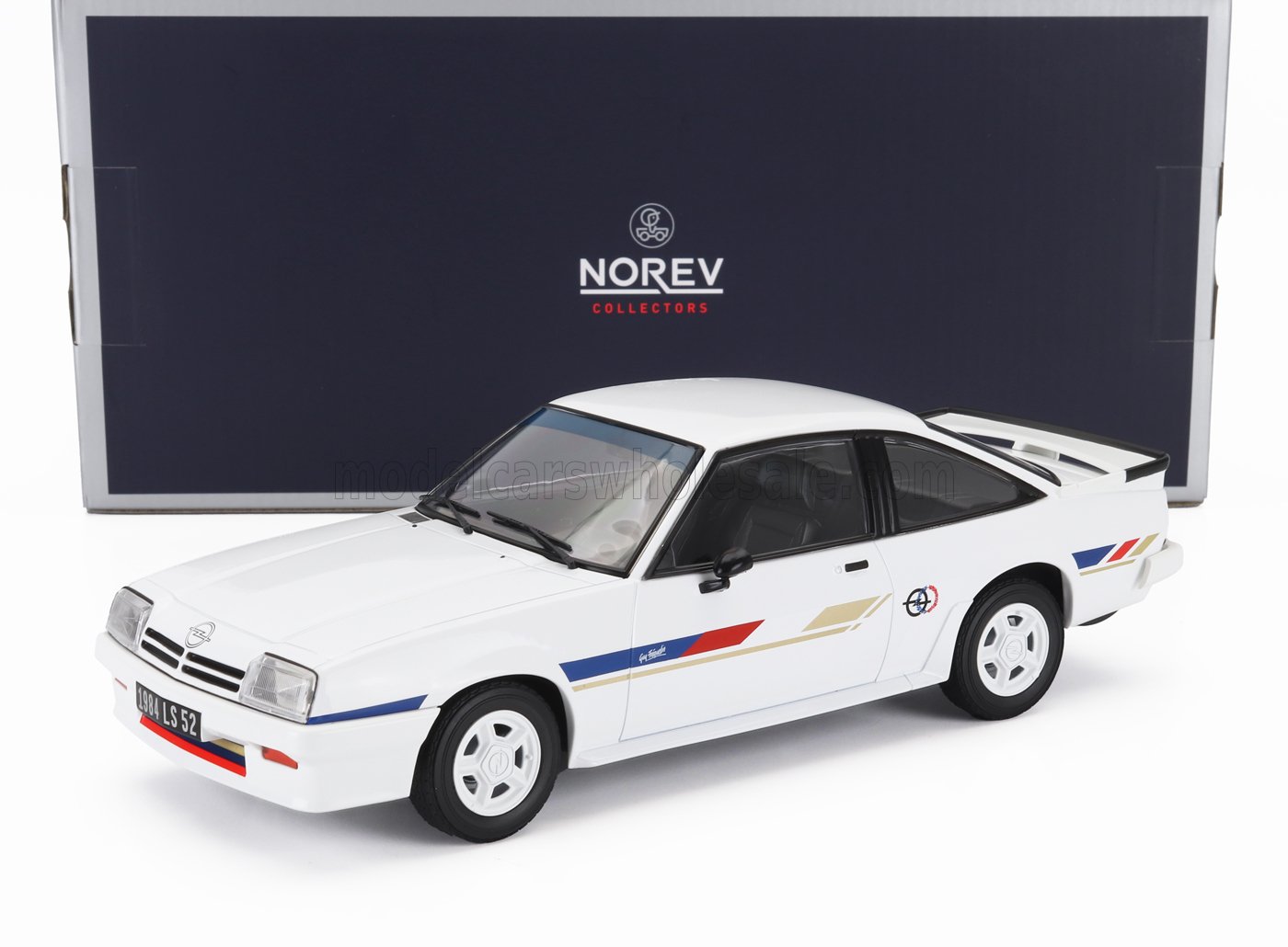 White 1984 Opel Manta model car with red, blue, and gold stripes, displayed in front of Norev Collectors box, sold on Vroomi