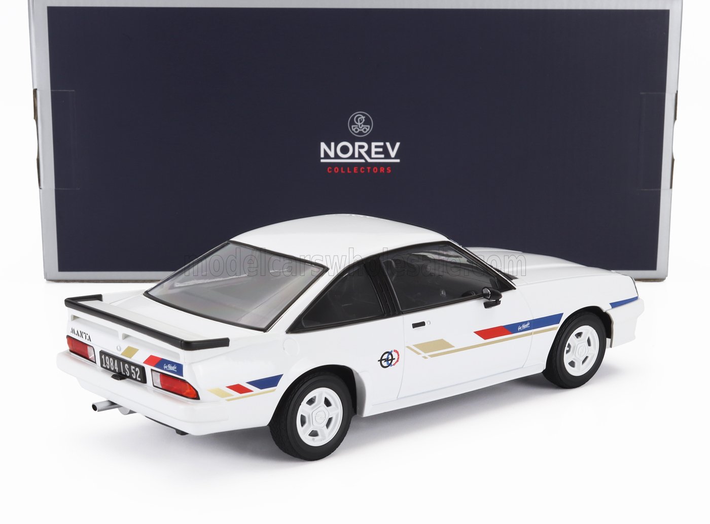 White Opel Manta model car with red, blue, and gold stripes, displayed in front of Norev Collectors box, also available on Vroomi