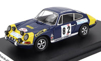 Coche a escala de rally Porsche 911 azul y amarillo con calcomanías de competición, sobre peana negra en Vroomi