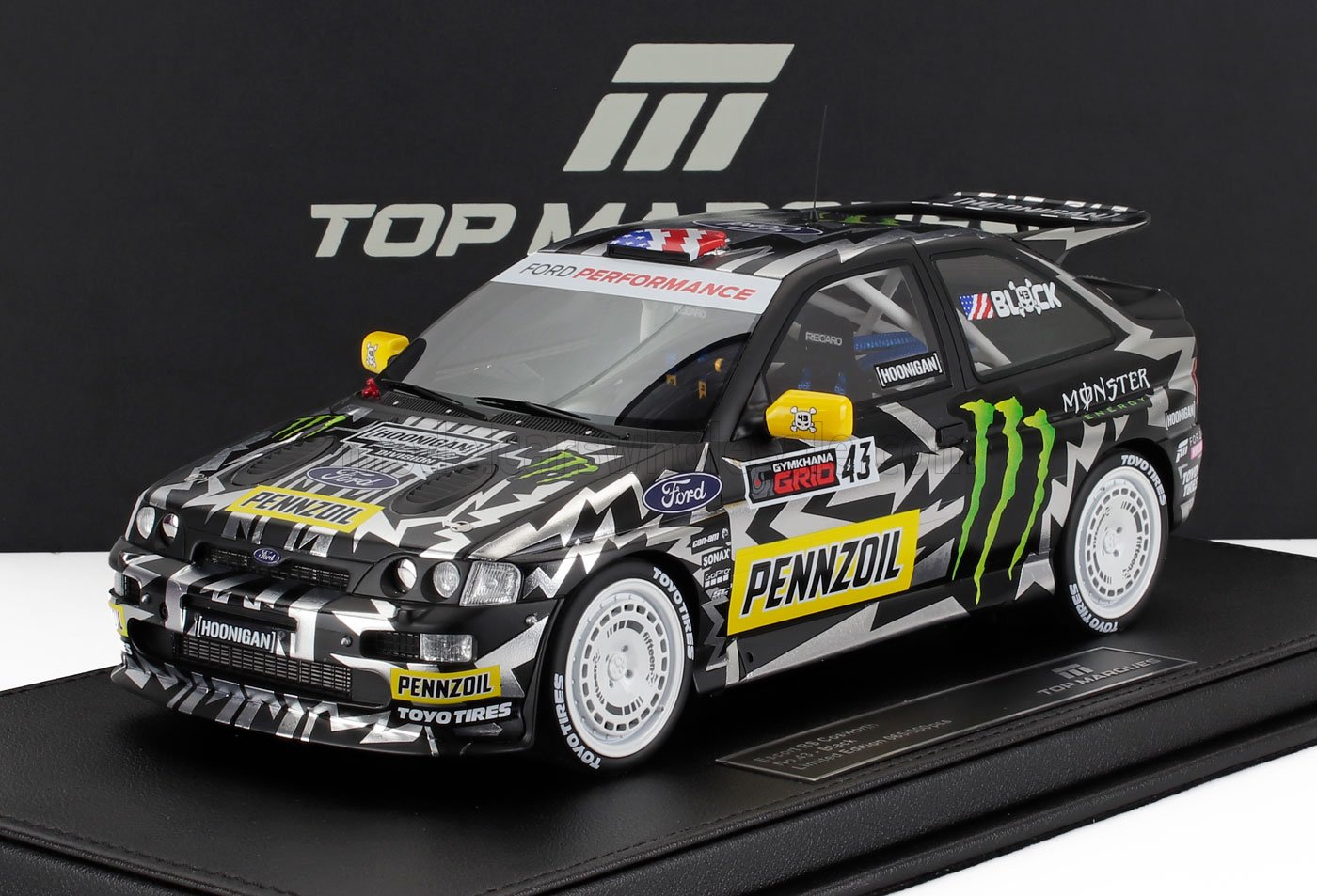 Black and white Ford Escort rally car model with Pennzoil and Monster logos, shown on display platform, also offered on Vroomi