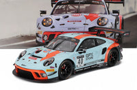 Coche a escala Porsche 911 GT3 R con decoración Gulf, expuesto ante el fondo de edición de coleccionista Vroomi