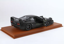 Matte black Ferrari F40 model car with open door on brown leather display base, available on Vroomi