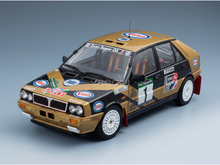 A scale model of a Lancia Delta Esso rally car of Tabaton-Tedeschini , featuring a gold and black livery with various racing sponsor decals, photographed on a clean gray gradient background.