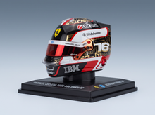 A collectible miniature Formula 1 helmet displayed on a black base. The helmet is for Charles Leclerc's 2025 Abu Dhabi GP, featuring a black, red, white, and gold livery with sponsor logos including Urtka, Bitdefender, and IBM.