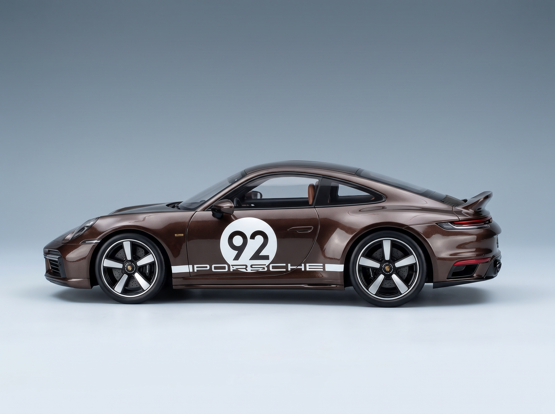 modellino , una Porsche 92 in scala, di colore marrone con strisce da gara bianche, presentata da Vroomi per i collezionisti.