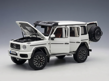 Weißes Mercedes-Benz G-Wagen-Modellauto mit geöffneten Türen und Motorhaube, präsentiert von Vroomi