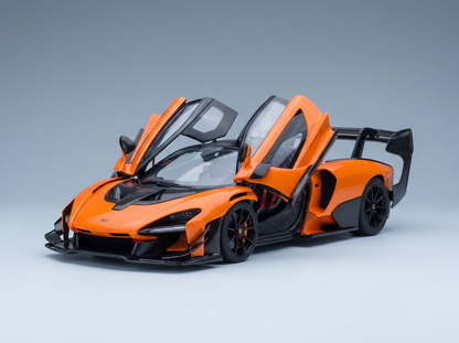 An orange and black scale model of a McLaren Senna supercar with its distinctive dihedral doors open, set against a clean gray studio background.