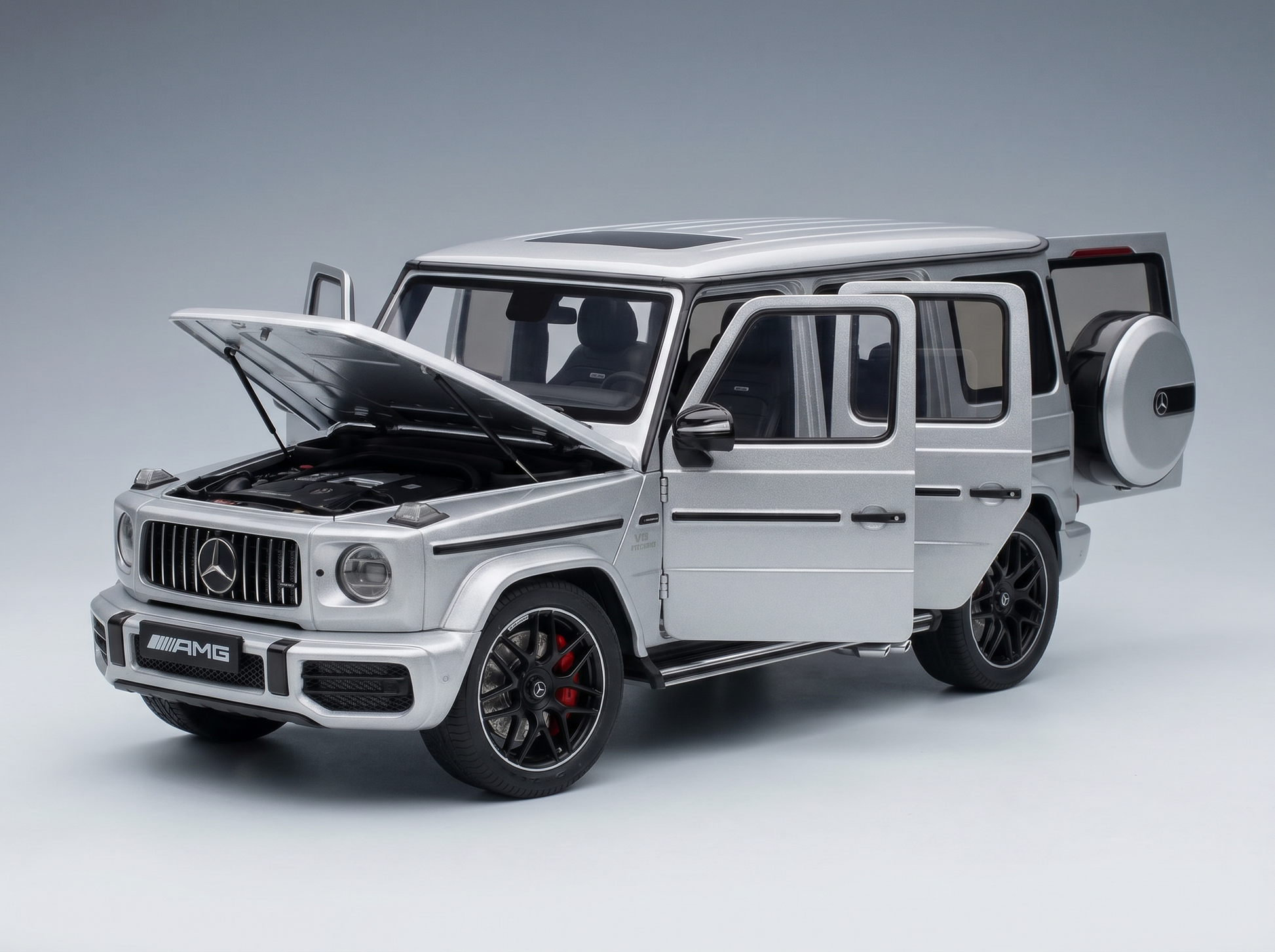 Silbernes Mercedes-AMG G63-Modellauto mit geöffneten Türen und Motorhaube sowie detailgetreuem Motor bei Vroomi