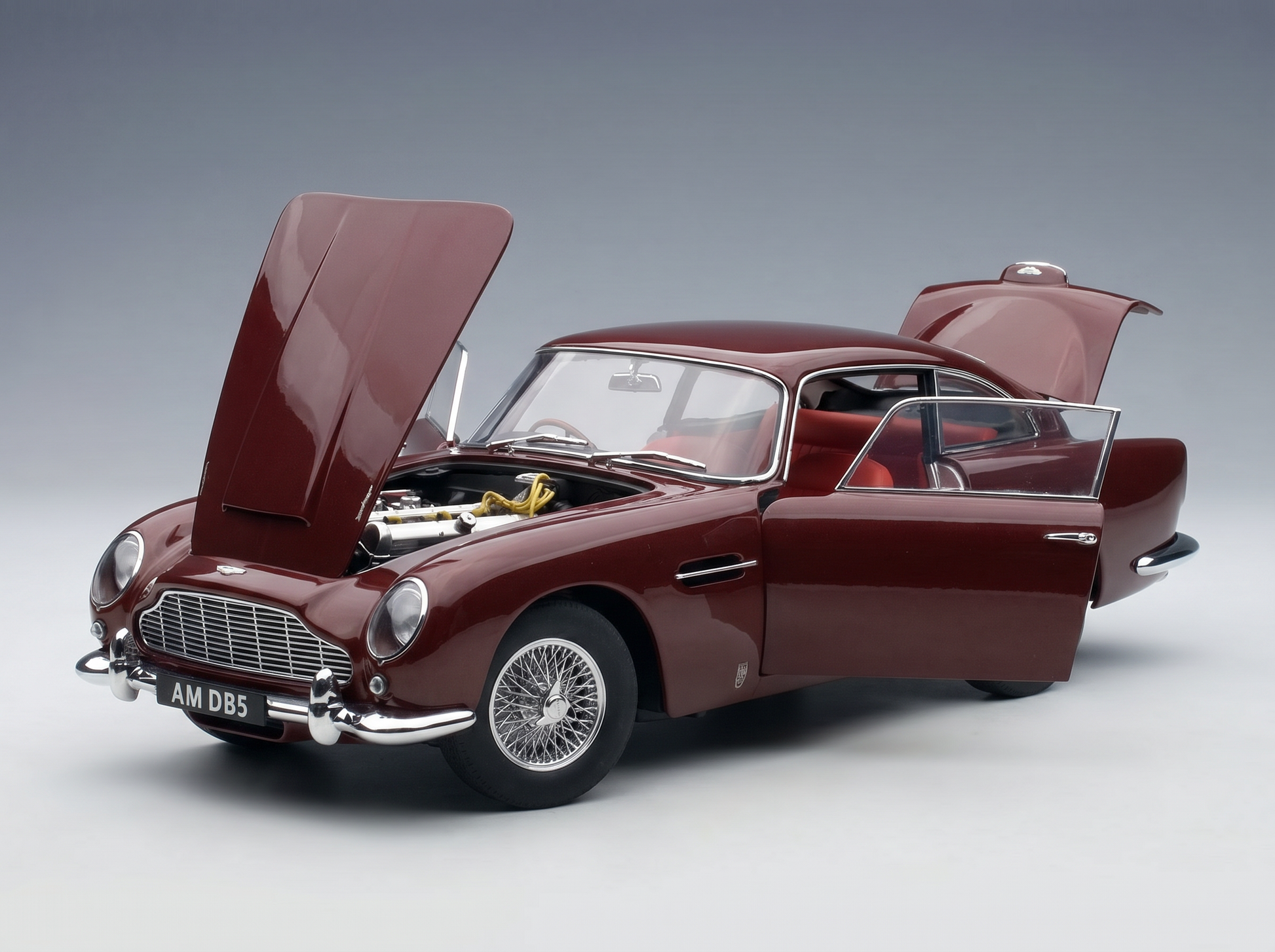Red Aston Martin DB5 scale model car with open hood and doors, showcased by Vroomi