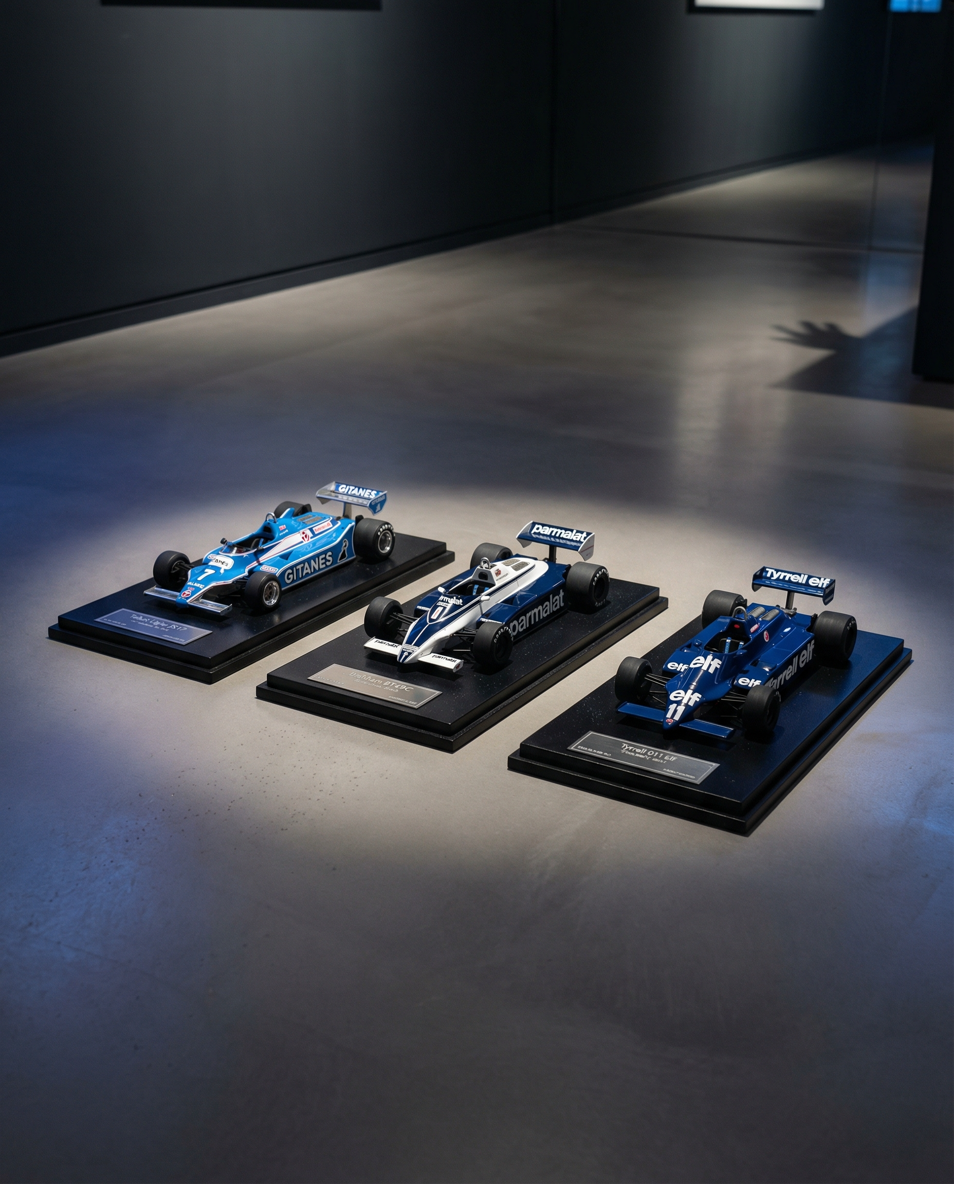 Three model racing cars on display stands in a dark room with spotlight effect.