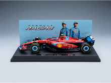 Maqueta a escala de un Ferrari rojo de Fórmula 1 de la marca Vroomi, con los logotipos de los patrocinadores y los nombres de los pilotos detallados en la base de exposición.