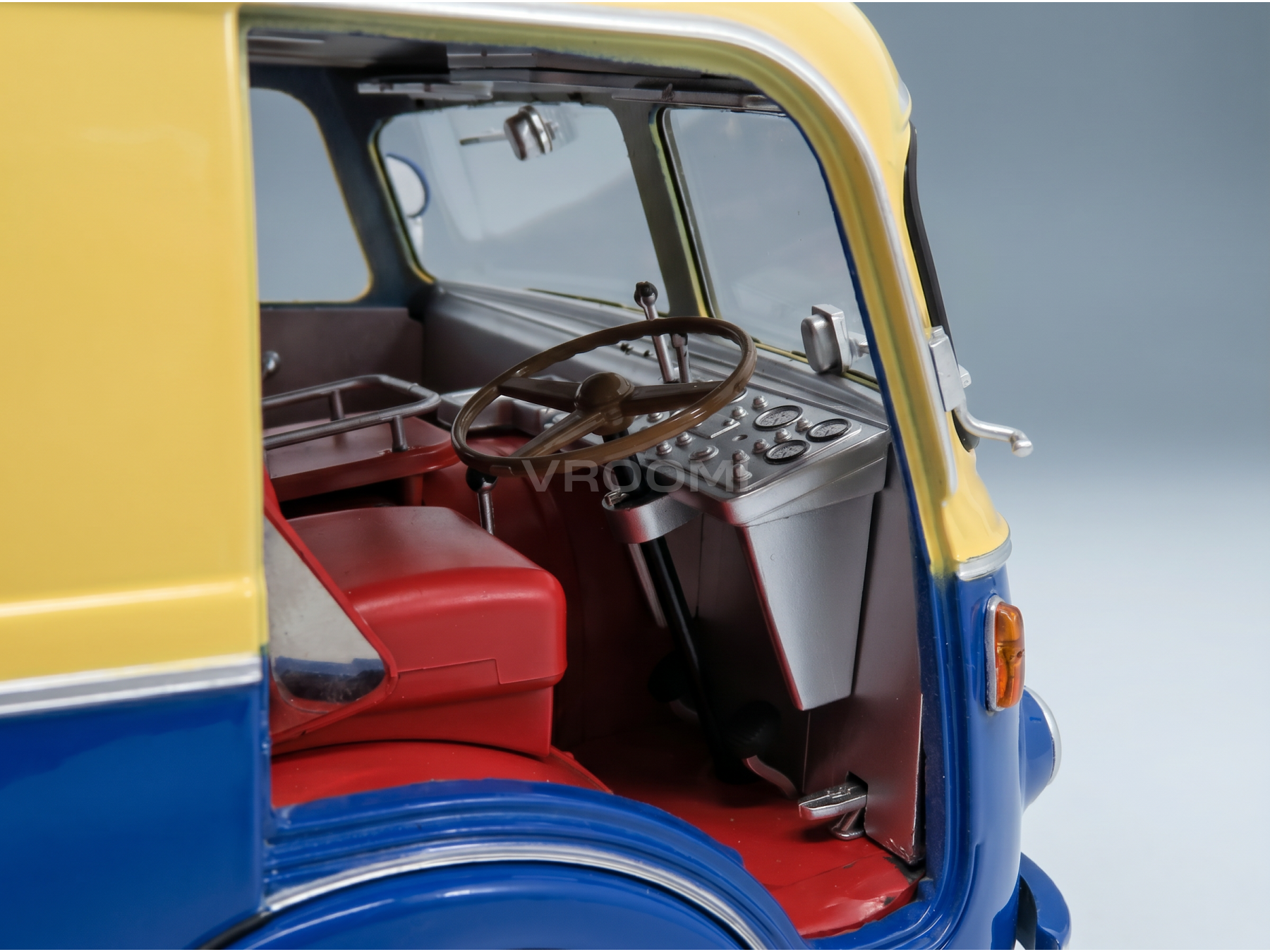 Gedetailleerd interieur van een blauw-geel schaalmodel van een auto, met rode stoelen en een rood dashboard, van Vroomi
