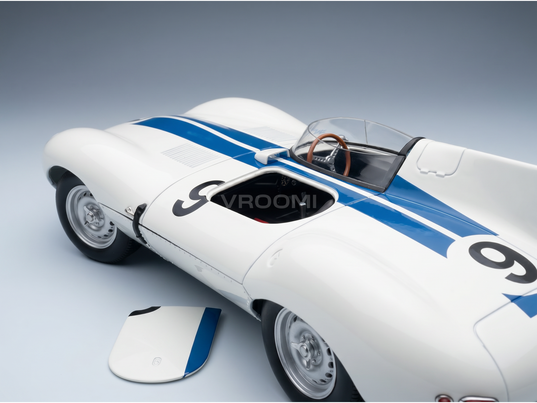 Modèle réduit de voiture de course blanche et bleue portant le numéro 9, proposé par Vroomi aux collectionneurs.