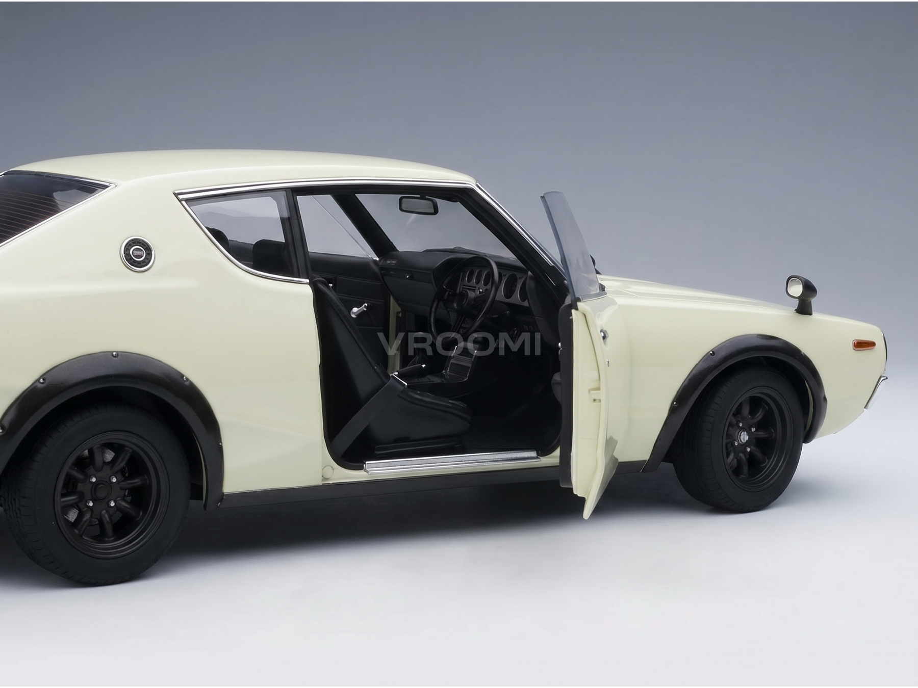 Crèmekleurig schaalmodel van een auto met open deur, gedetailleerd interieur, zwarte wielen en Vroomi-logo