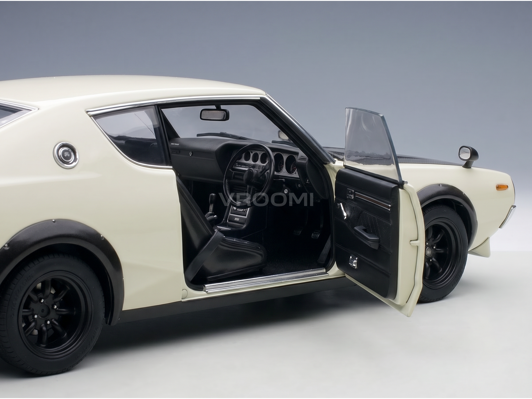Crèmekleurig schaalmodelauto met open deur, gedetailleerd interieur en zwarte wielen, gepresenteerd door Vroomi