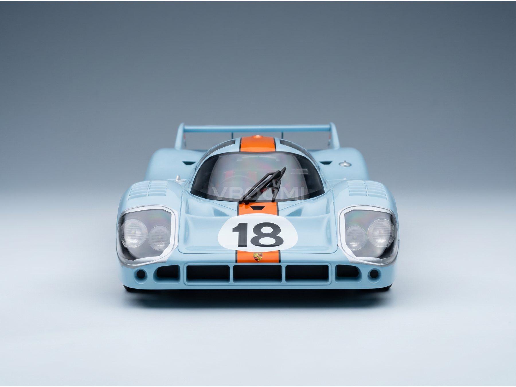 Maqueta a escala de un Porsche 917K de color azul claro con rayas naranjas y el número 18, presentada por Vroomi