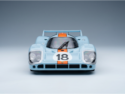 Maqueta a escala de un Porsche 917K de color azul claro con rayas naranjas y el número 18, presentada por Vroomi
