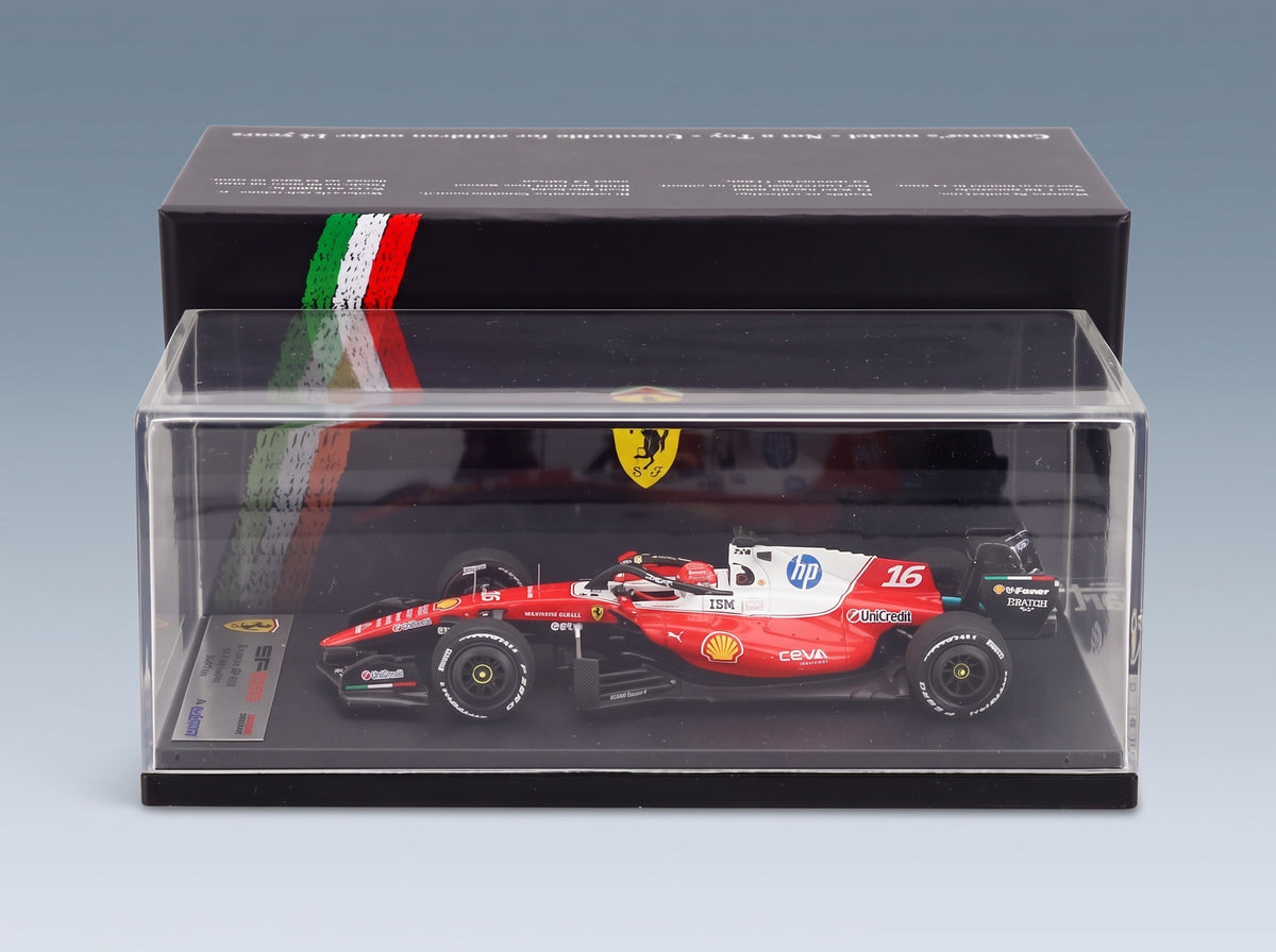 A red and white Ferrari F1 2025 car model displayed inside a clear plastic showcase box with a black base, set against a dark display stand with the Italian flag and Ferrari shield.