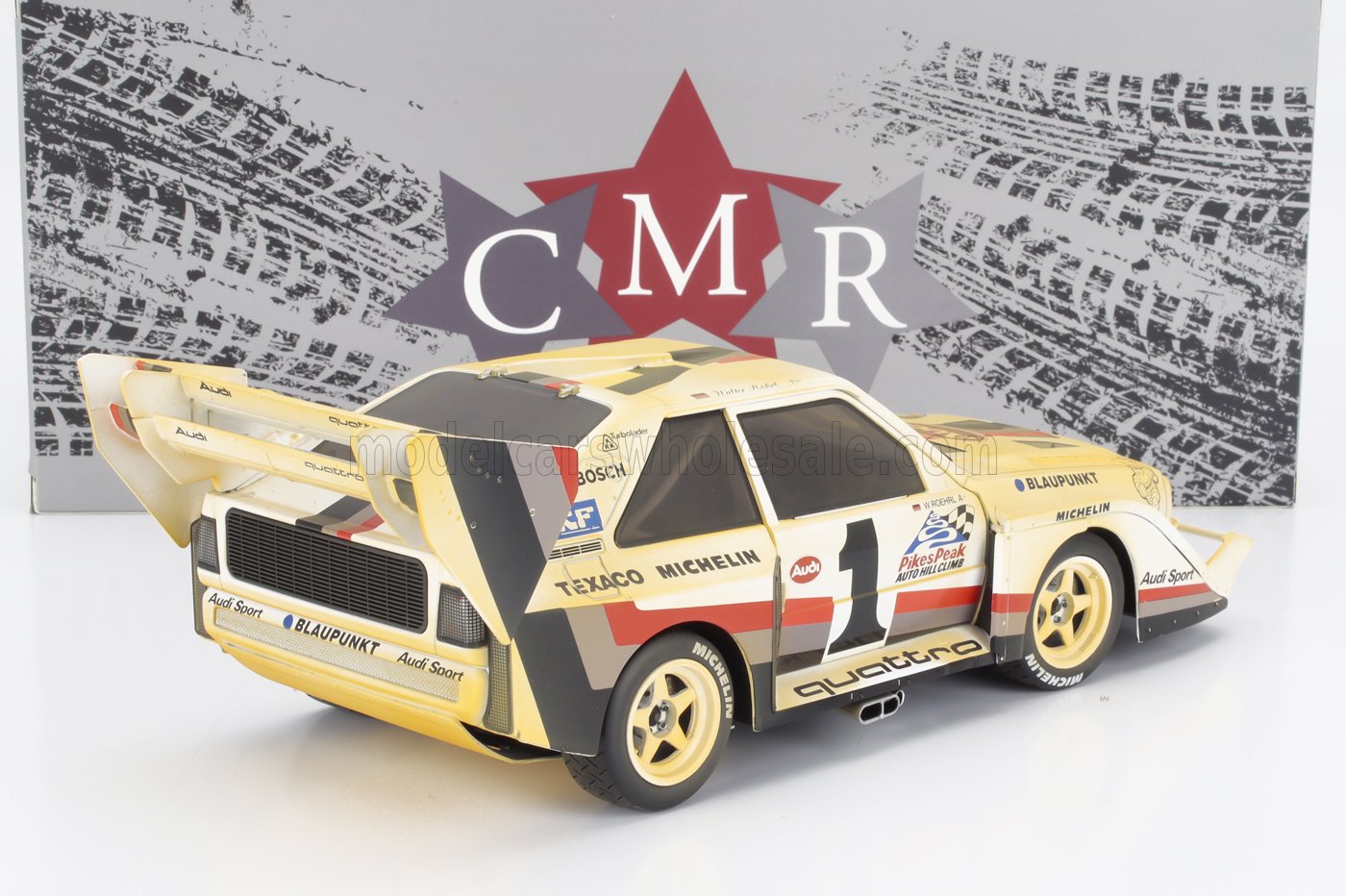 Modelo de coche de rally Audi Quattro amarillo con adhesivos de competición, alerón trasero grande y neumáticos Michelin, ofrecido a través de Vroomi.