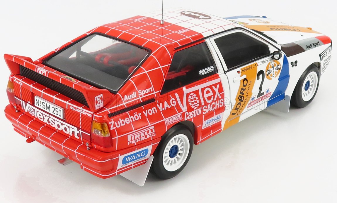 Modelo a escala 1/18 del coche de rally Audi con decoración roja, blanca y azul, disponible en Vroomi.