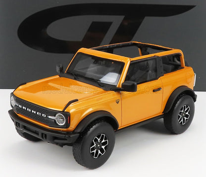 Coche a escala 1/18 de Orange Ford Bronco con ruedas negras, techo abierto, expuesto sobre una superficie blanca, disponible en Vroomi.