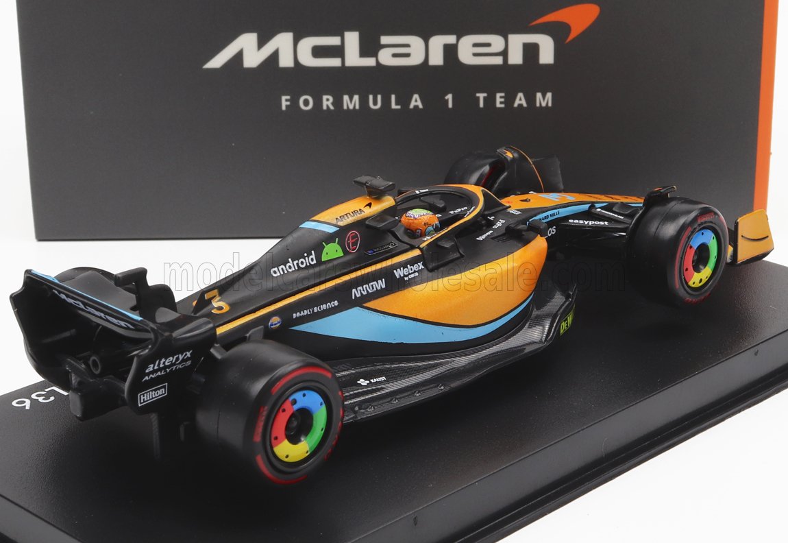 Coche de carreras McLaren de Fórmula 1 con diseño en negro y naranja, neumáticos arcoíris, expuesto sobre una base negra, disponible en Vroomi.