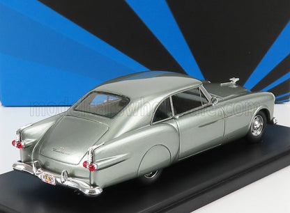 Coche clásico plateado de los años 50 en un expositor con fondo geométrico azul, a la venta en Vroomi.