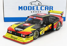 Coche de carreras Ford Zakspeed Turbo negro, rojo y amarillo con la marca Mampe y un gran alerón trasero, disponible en Vroomi.