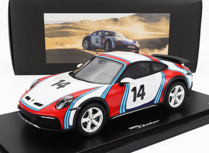 Modelo a escala de Porsche 911 Dakar con el número 14 y colores rojo, blanco y azul, mostrado con un fondo desértico, disponible a través de Vroomi.