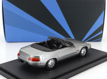 Silver Porsche 928 convertible model car on display stand with blue geometric background, available on Vroomi