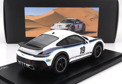 Coche de juguete Porsche 911 Dakar blanco con el número 19 y rayas azules de carreras en exhibición, disponible en Vroomi.