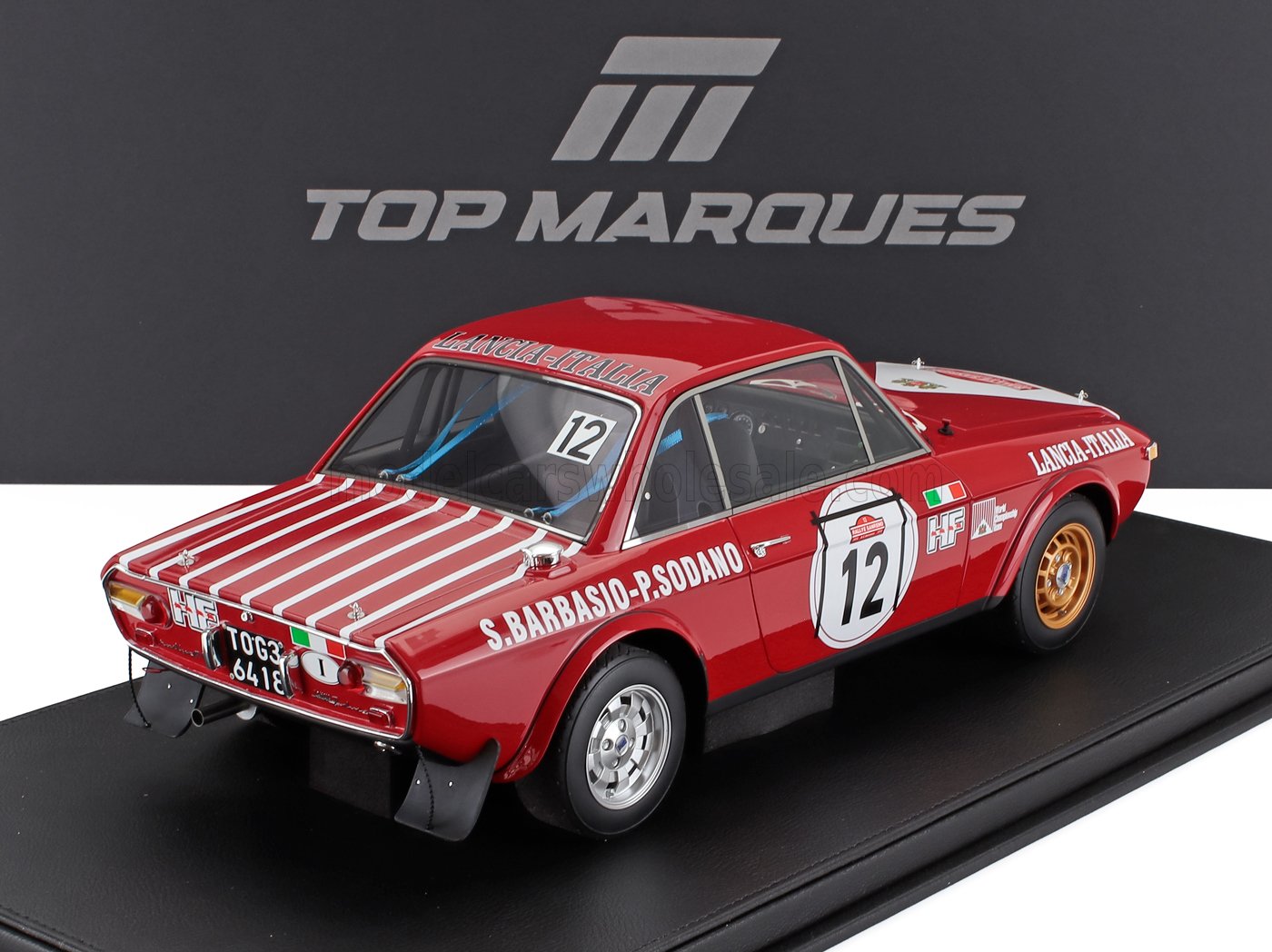 Modelo de coche de rally Lancia rojo con el número 12 y adhesivos de carreras con el logotipo de Top Marques, ahora disponible en Vroomi.