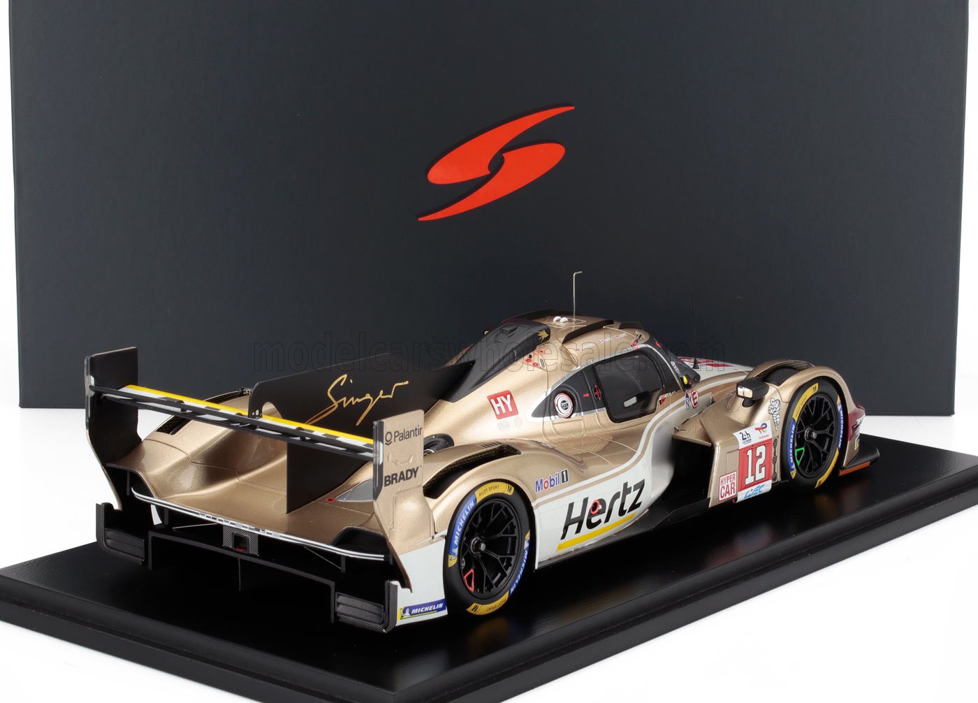 Maqueta de un coche de carreras Hertz dorado y blanco con el número 12 en un expositor, presentado en la plataforma Vroomi.