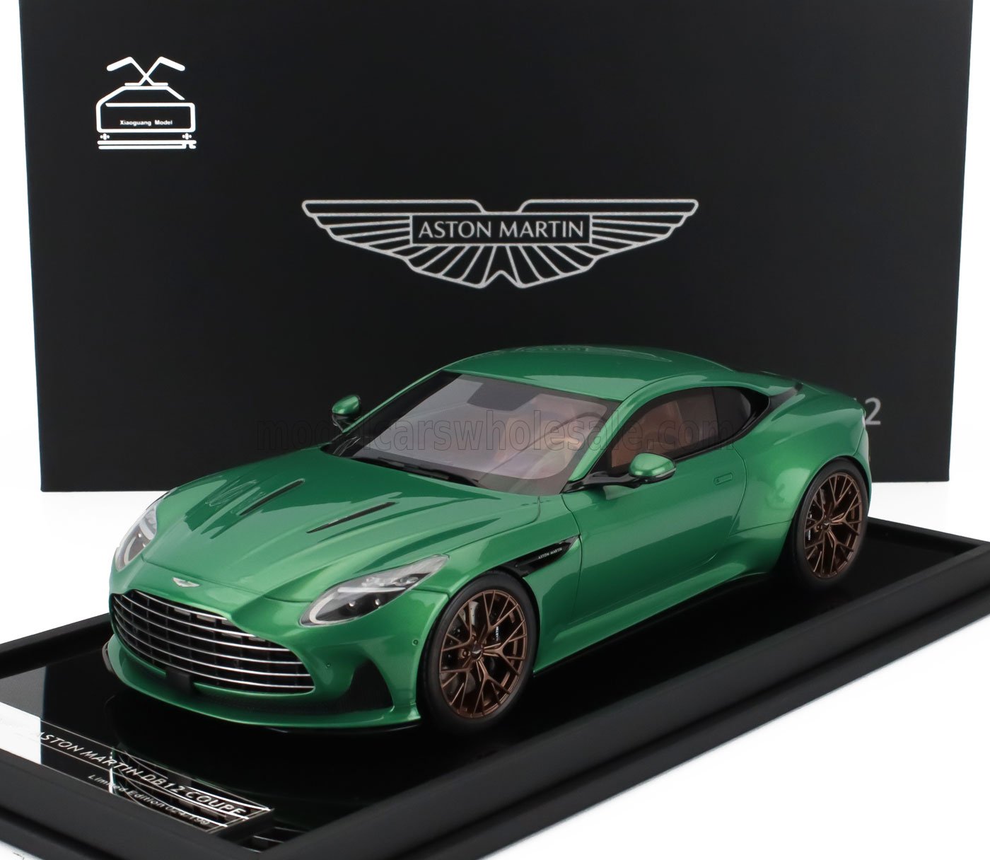 Modelo de coche Aston Martin DB11 verde con llantas de bronce expuesto sobre una base negra, disponible en Vroomi.