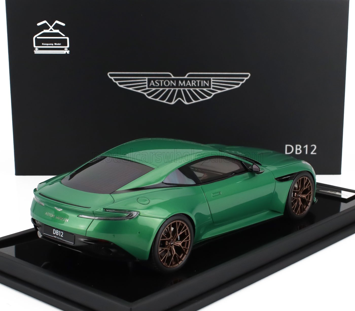 Modelo de coche Aston Martin DB12 verde con llantas de bronce expuesto sobre una plataforma negra, a la venta en Vroomi.