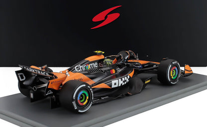 Modelo de coche de Fórmula 1 McLaren en negro y naranja con logotipos de patrocinadores, presentado como disponible en la plataforma Vroomi.
