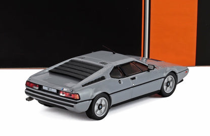 Modelo de coche deportivo BMW M1 gris con rejillas negras, presentado sobre un fondo naranja y negro, disponible en Vroomi.