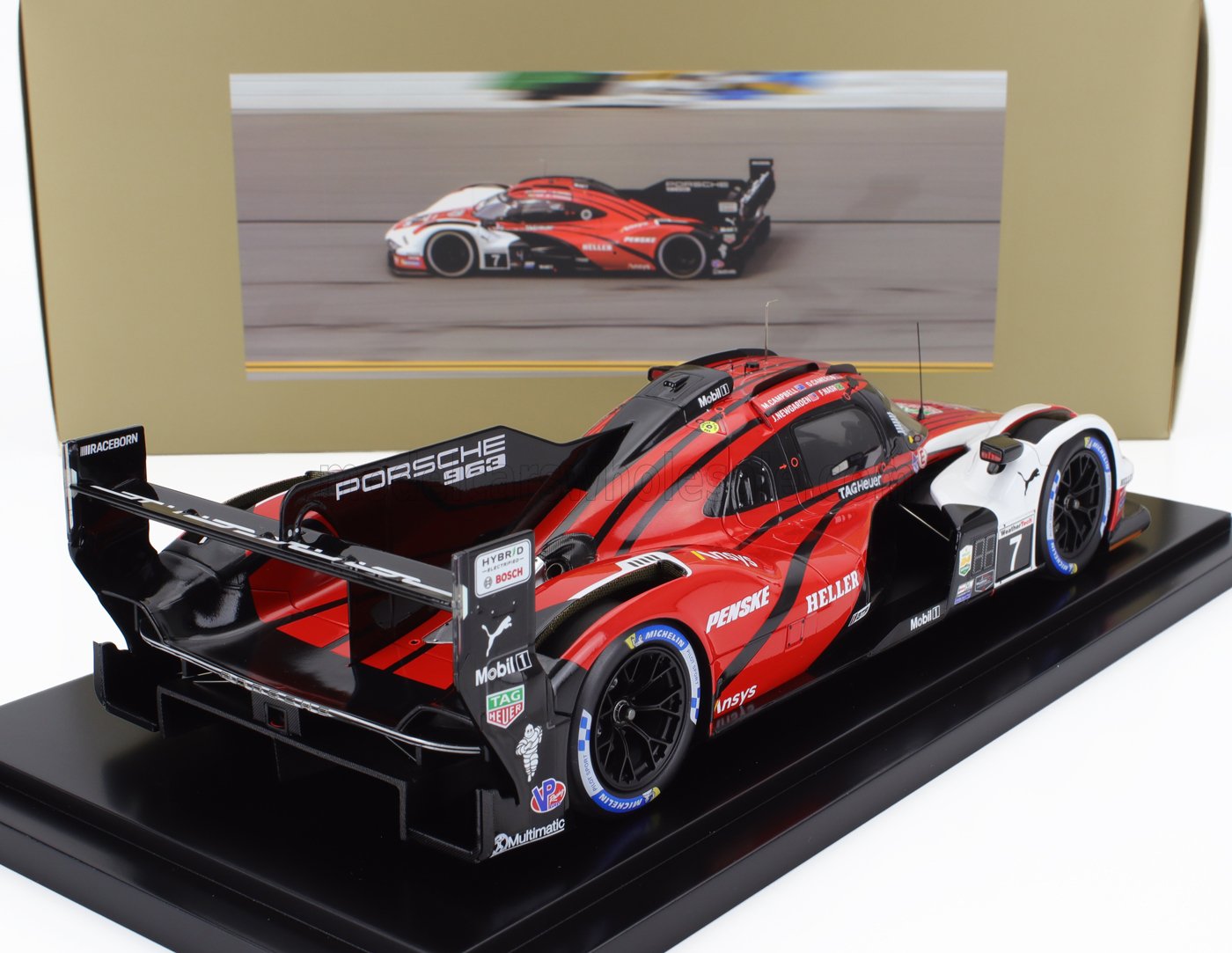 Modelo de coche de carreras Porsche 963 rojo y negro en un expositor con foto de fondo, disponible a través de Vroomi.