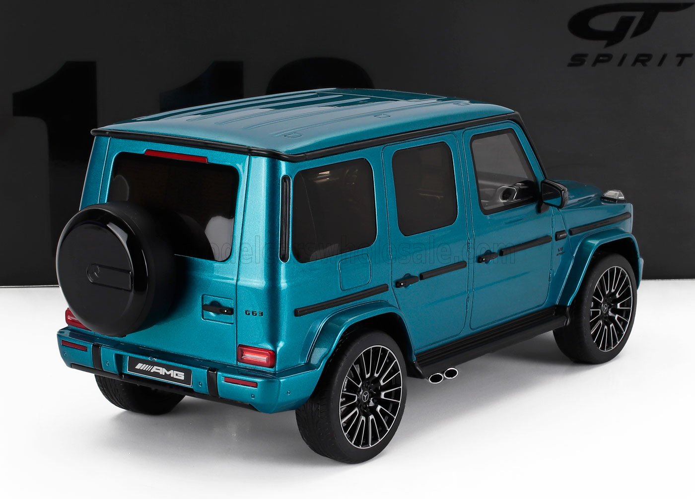 Coche en miniatura Mercedes-Benz G63 AMG de color verde azulado a escala 1/18 sobre superficie blanca con fondo negro, disponible en Vroomi.