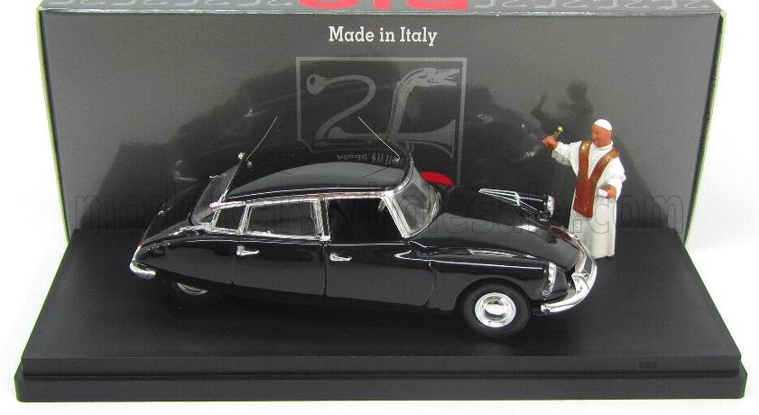 Coche de colección negro con una figura de una persona vestida con túnicas blancas en un expositor, disponible en Vroomi.