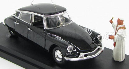 Modelo clásico de coche vintage negro con detalles plateados y una figurita de un sacerdote bendiciéndolo, disponible en la plataforma Vroomi.