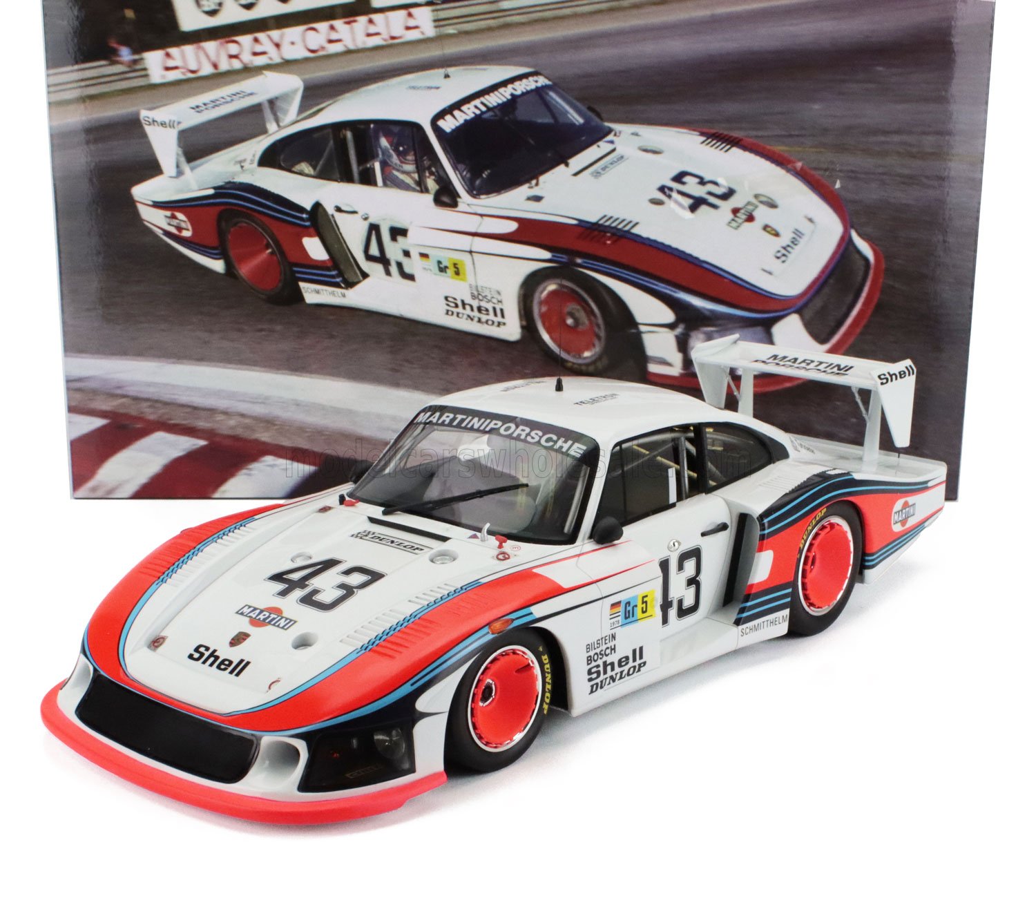 Modèle réduit de voiture de course Porsche 935 Martini blanche et rouge portant le numéro 43, exposé devant une affiche de course, sur Vroomi.