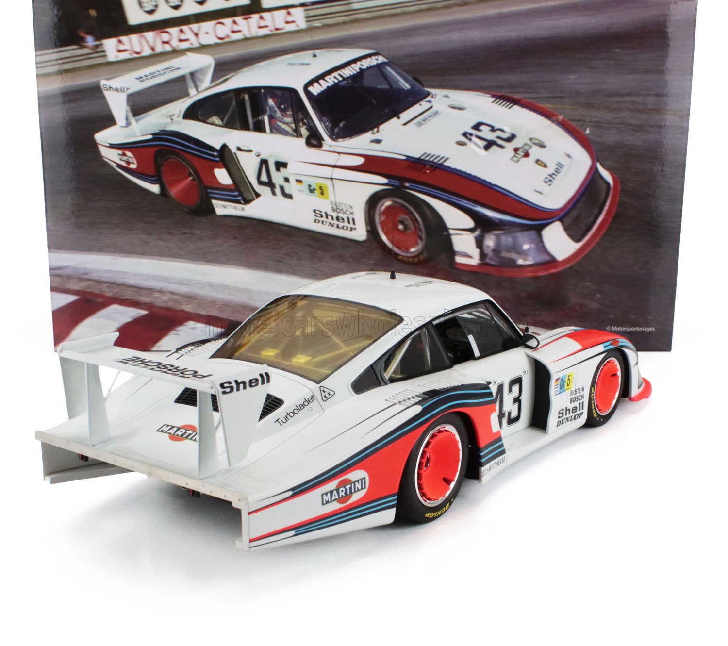 Modèle réduit de voiture de course Porsche 935 Martini blanche avec roues rouges et logos des sponsors, accompagné d'une photo historique de course, disponible sur Vroomi.