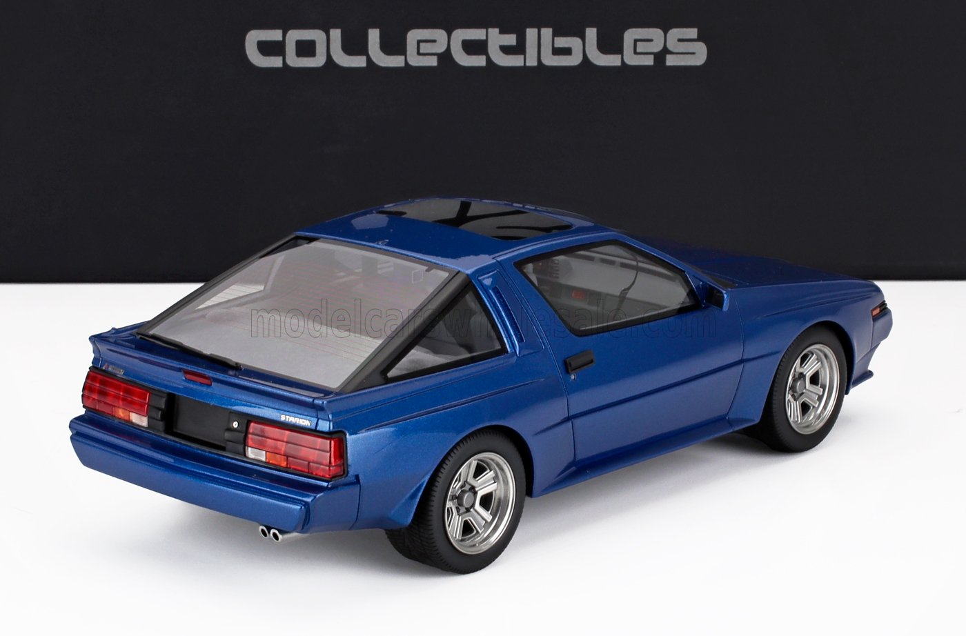 Modèle réduit bleu d'une voiture de sport à hayon des années 1980, présenté sur un fond blanc avec un décor Collectibles, désormais disponible sur Vroomi.