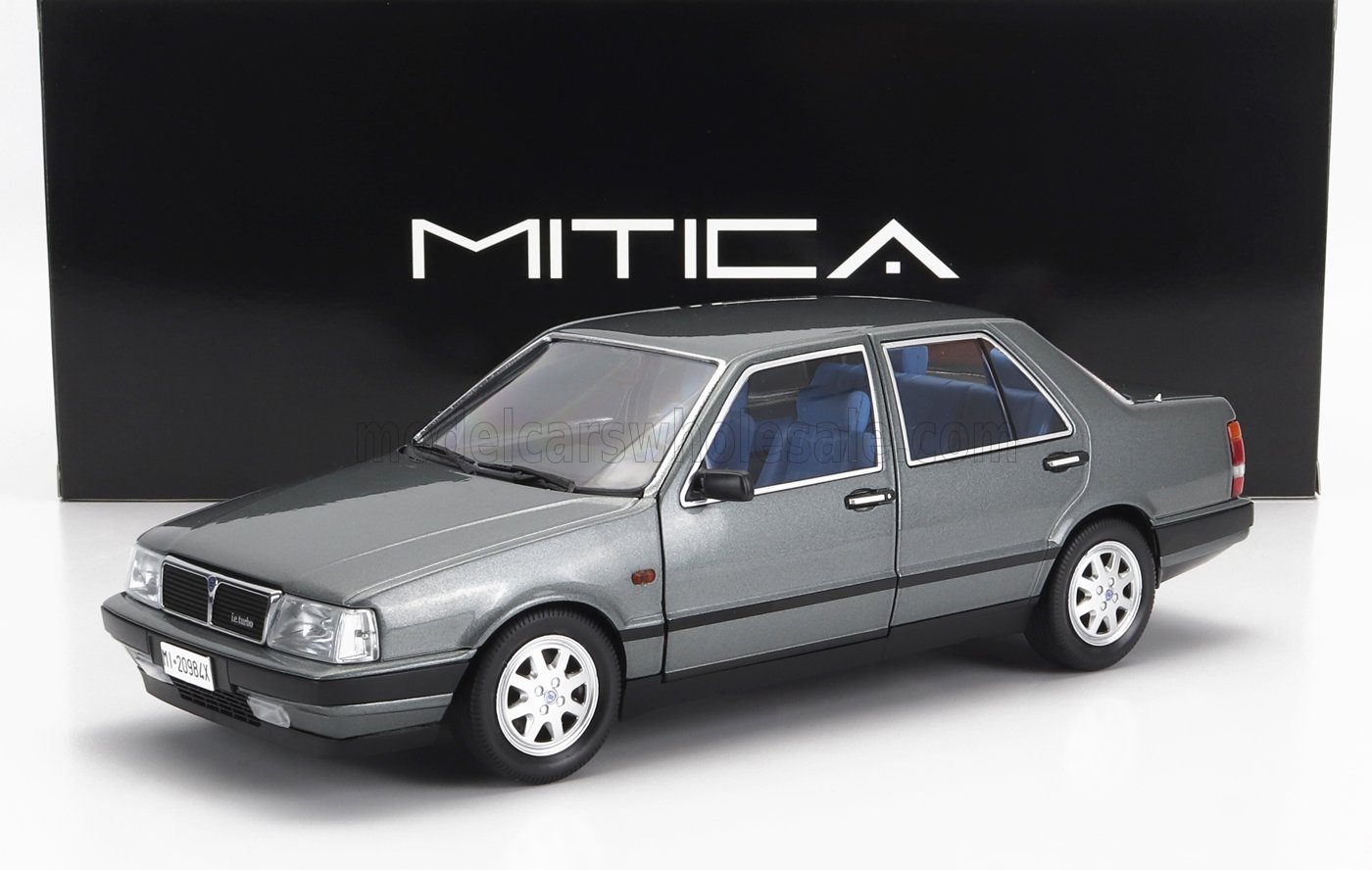 Modèle réduit de voiture Lancia Thema IE Turbo grise avec intérieur bleu, exposée devant une boîte MITICA noire, disponible sur Vroomi.