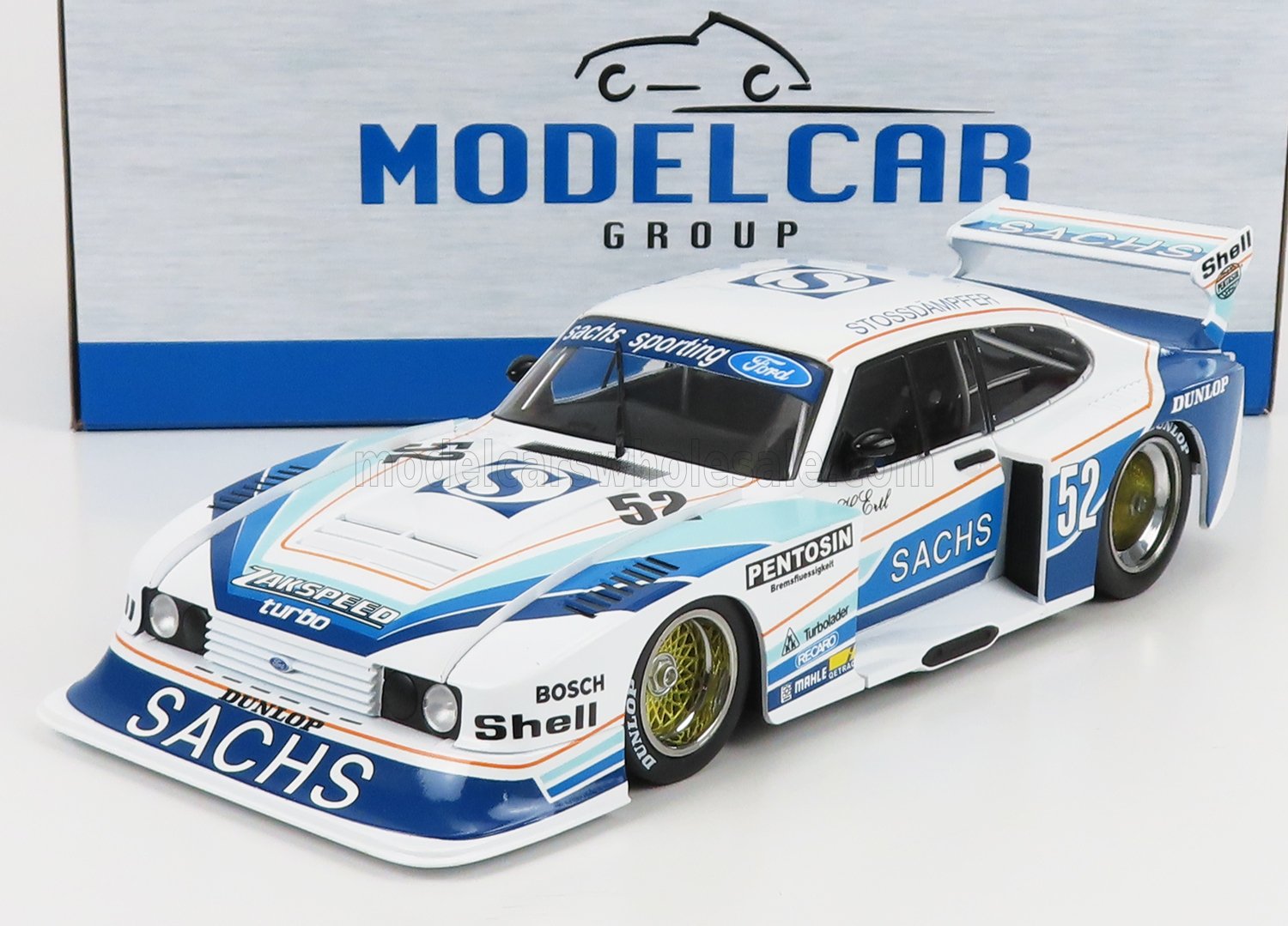 Modèle réduit de voiture de course Ford à l'échelle 1/18, blanc et bleu, avec les logos Sachs et Shell, présenté dans une boîte Modelcar Group, disponible chez Vroomi.