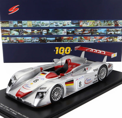 Modèle réduit en argent de l'Audi Le Mans 24 heures avec accents rouges, sponsors détaillés, sur socle noir, présenté avec des affiches historiques de la course, désormais disponible sur Vroomi.
