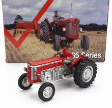 Maquette du tracteur rouge Massey Ferguson 65 Mark II devant un décor agricole vintage avec un vrai tracteur et des balles de foin, disponible chez Vroomi.