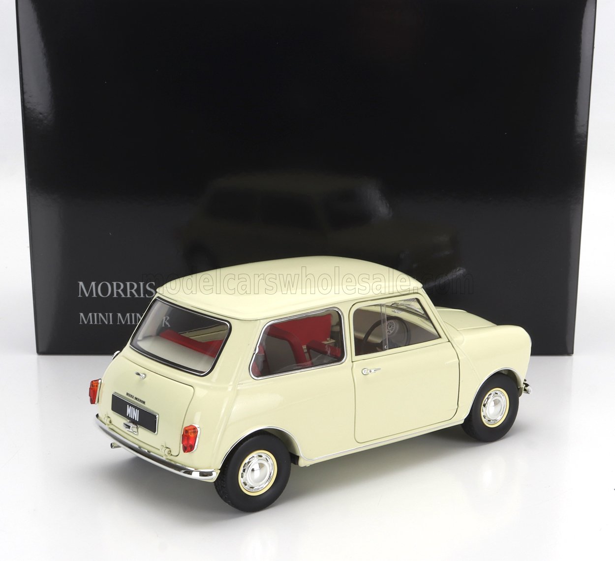 Modèle réduit Cream Morris Mini Minor avec intérieur rouge, exposé devant une boîte noire, disponible chez Vroomi.